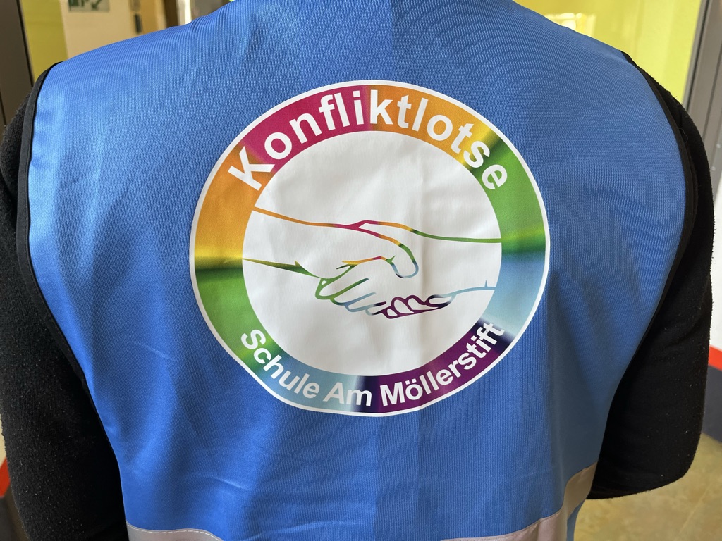 Die blaue Weste mit dem Logo: sich reichende Hände in regenbogenfarben