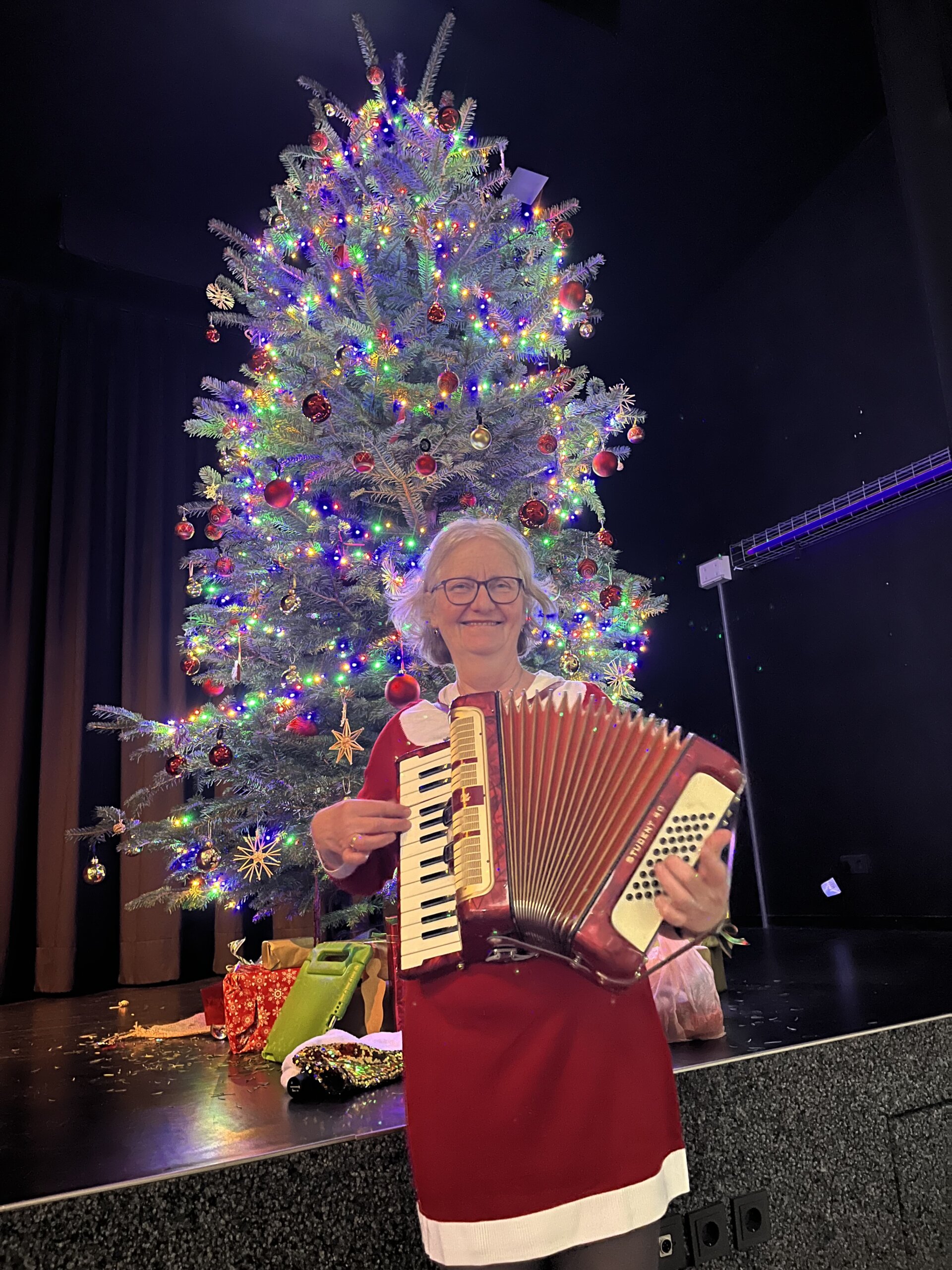 Frau Rogalski steht mit ihrem Akkordeon vor dem Weihnachtsbaum